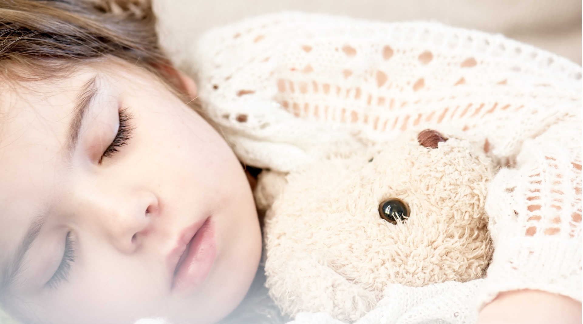 Mädchen schläft friedlich mit Teddy im Arm